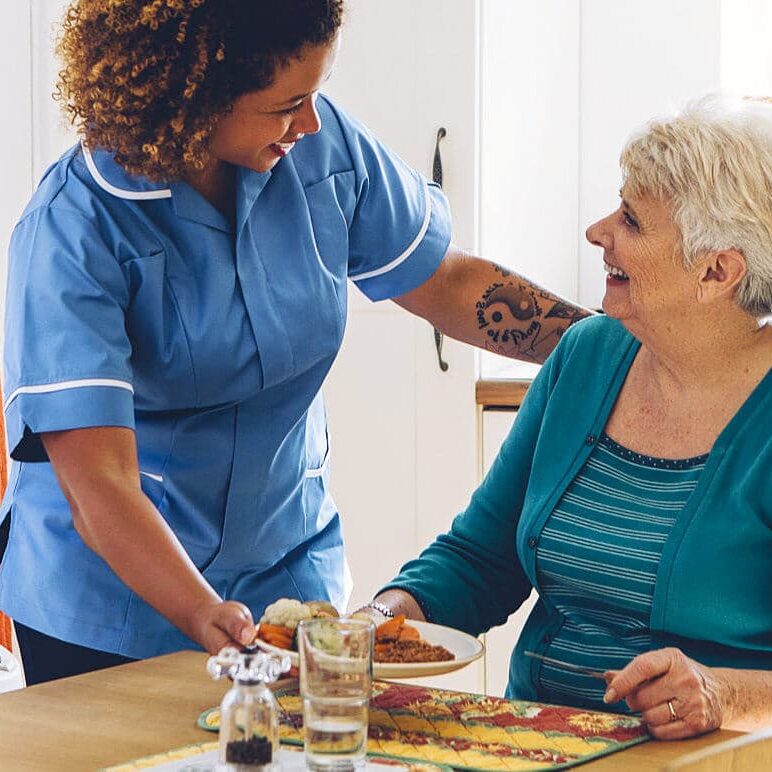 Meal Preparation 1 Care nurse serving dinner to a senior woman at home